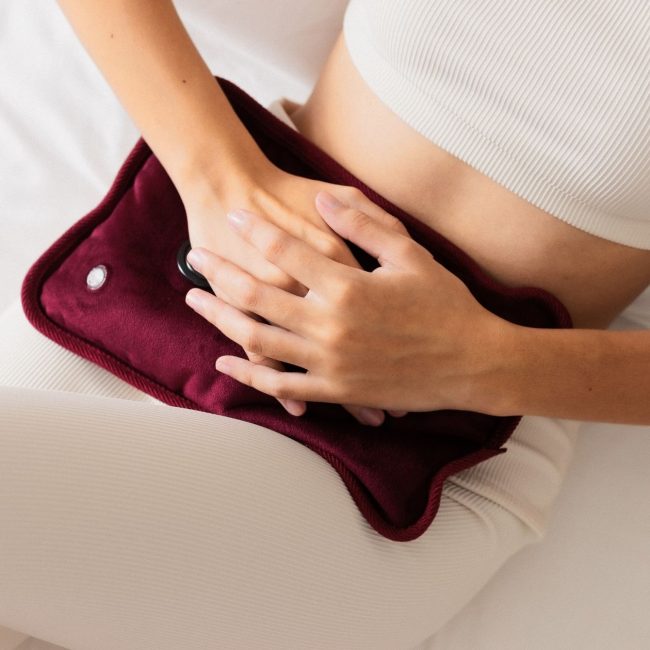 infrared sauna during your period_ girl with menstrual cramps applying hot compress on belly